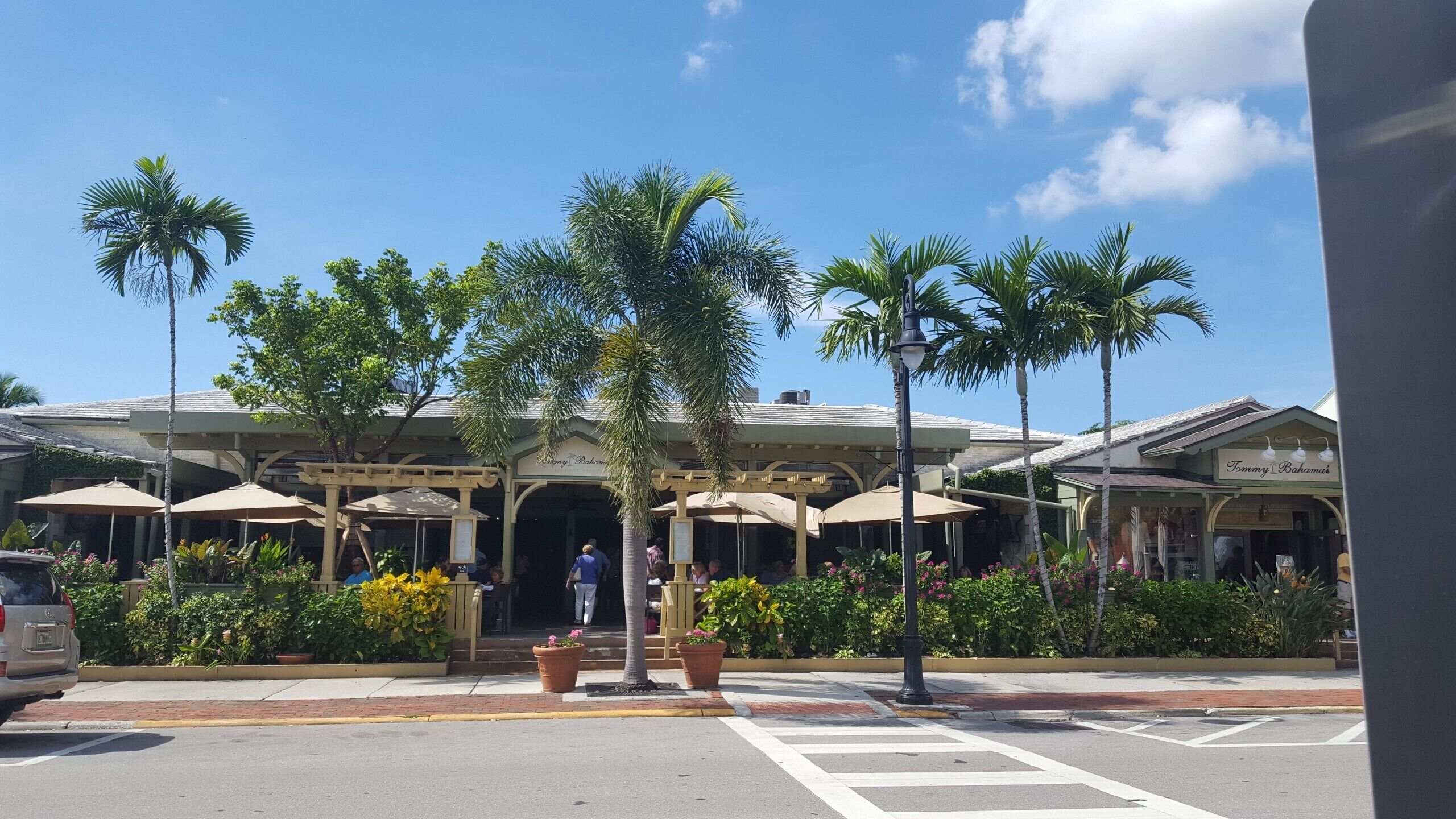 Un bâtiment doté d’une entrée couverte, d’une terrasse avec des parasols et de palmiers.