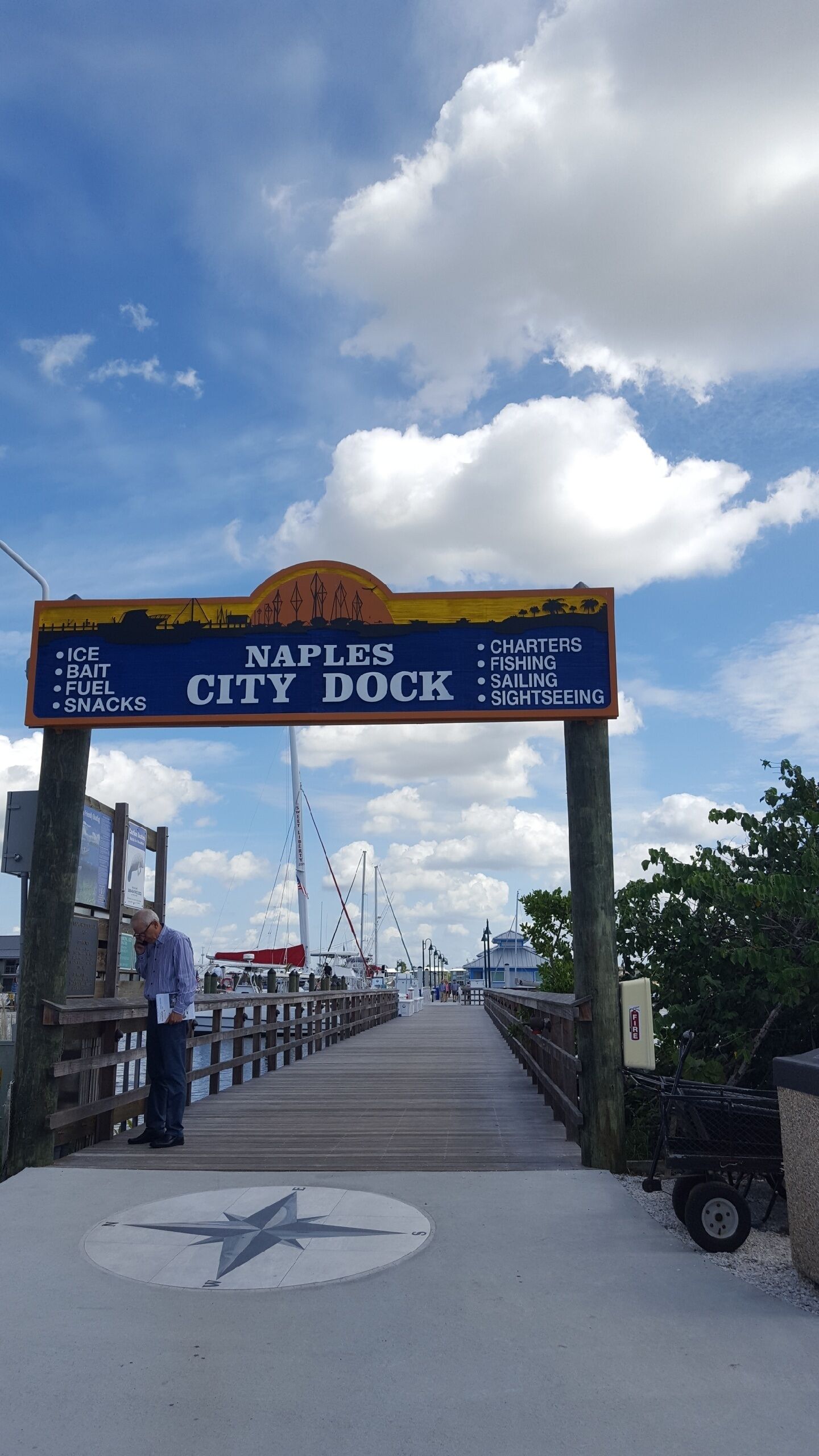 A sign for the Naples City Dock offering ice, bait, fuel, snacks, charters, fishing, sailing, and sightseeing.