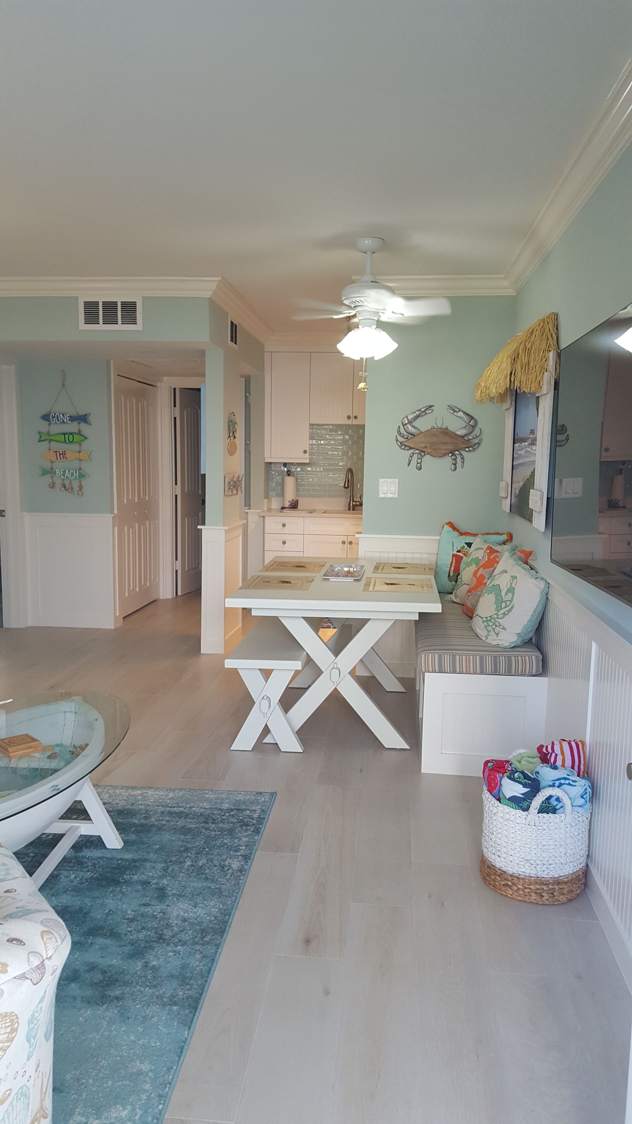 A spacious living area with a dining table, a comfortable seating area, a kitchen in the background, and a ceiling fan.