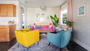 Ein modernes Wohnzimmer mit einer Couch, zwei Sesseln, einem Couchtisch und einer Küchenzeile mit Holzschränken.