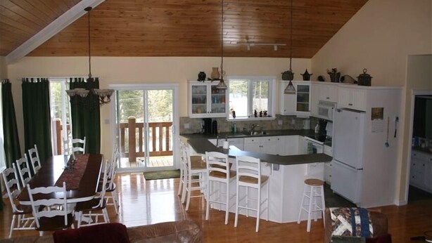 A spacious kitchen with white cabinets, a central island, and a dining area with a long table and chairs. - Luxury Panorama home on the hill (Panorama)