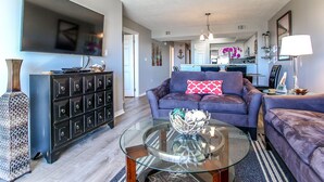 A modern living room with a flat-screen TV, a glass coffee table, and a dark-colored sofa. - 🦩Book Me Baby! Gulf-Front Condo With Gorgeous Views 🦩 (Fort Walton Beach)