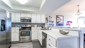 A modern kitchen with white cabinets, stainless steel appliances, and a checkered backsplash. - 🦩Book Me Baby! Gulf-Front Condo With Gorgeous Views 🦩 (Fort Walton Beach)