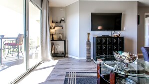 A modern living room with a large TV, a glass coffee table, and a view of a balcony. - 🦩Book Me Baby! Gulf-Front Condo With Gorgeous Views 🦩 (Fort Walton Beach)
