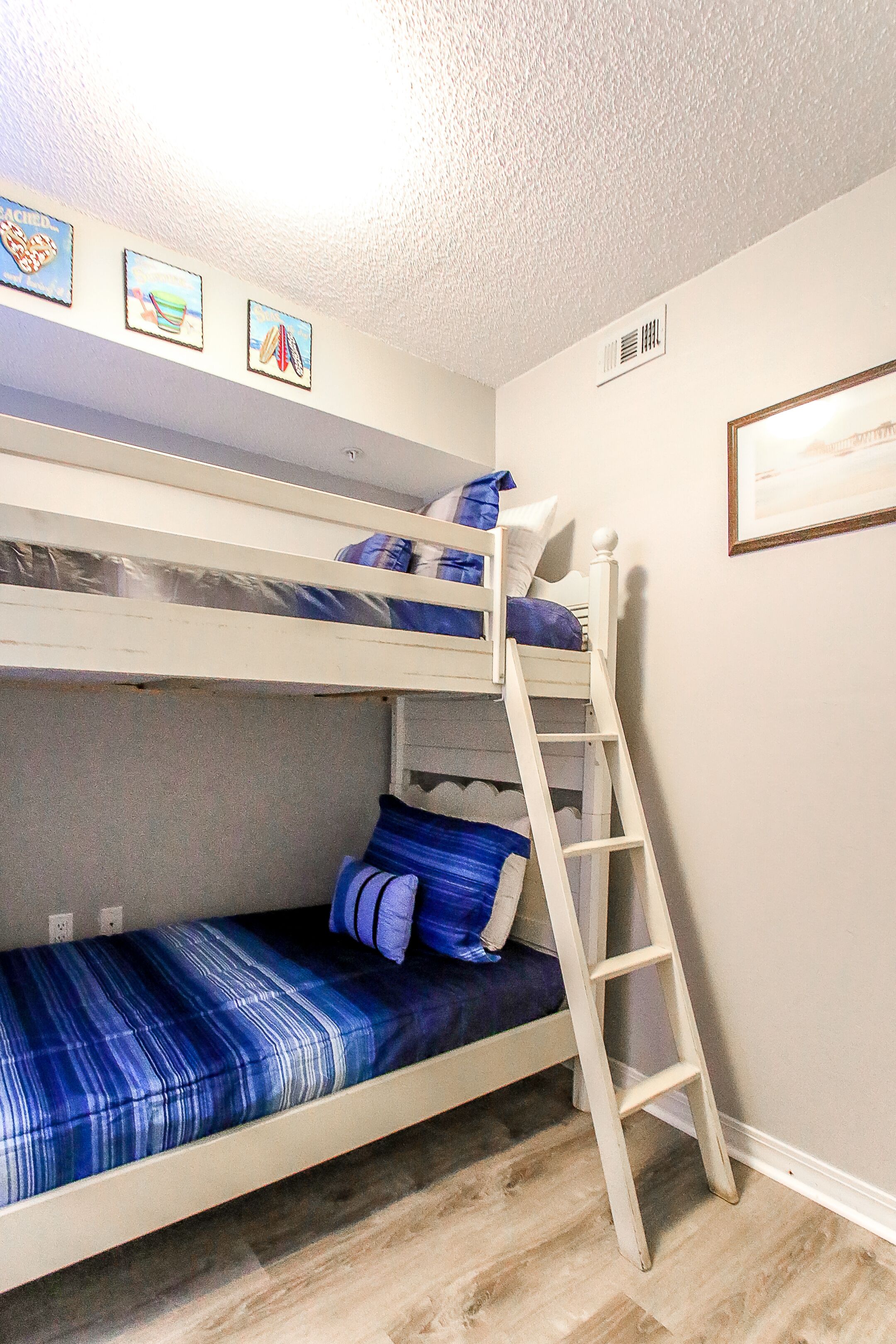 A bunk bed with a ladder, a blue and white striped bedspread, and a framed picture on the wall.
