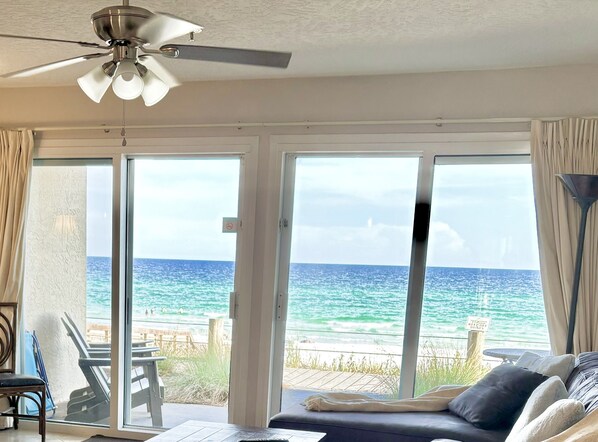 A room with a ceiling fan, a view of the ocean through large sliding glass doors, a sofa, and a table with chairs.