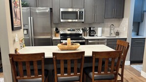 A modern kitchen with dark cabinets, stainless steel appliances, and a wooden dining table with chairs. - Remodeled 1 Bedroom Condo Short walk to Cabriolet Mountain views from unit (Park City)