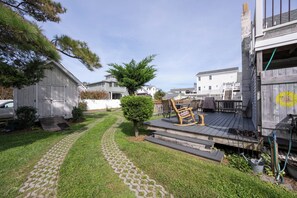 A residential area with a paved pathway leading to a wooden deck with outdoor furniture.