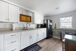 Una cocina con armarios blancos, un refrigerador negro, un lavamanos de acero inoxidable y una ventana con vista a una casa.