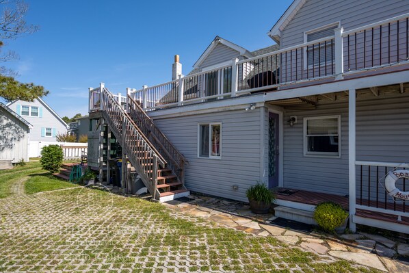 A two-story house with a wooden staircase leading to the upper floor, a covered porch with a lifebuoy, and a stone-paved driveway.
