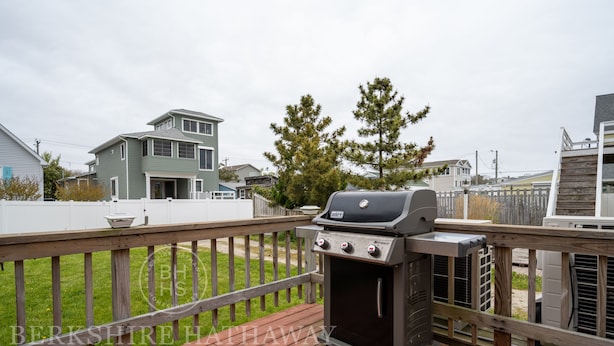 A deck with a barbecue grill, surrounded by a wooden fence and houses in the background.