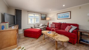 A living room with a red sofa, a wooden coffee table, a grey armchair, a television, and a bookshelf.