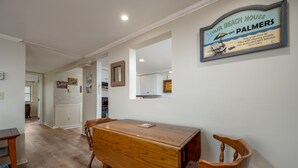 A dining area with a wooden table and chairs, a kitchen in the background, and a framed sign on the wall.
