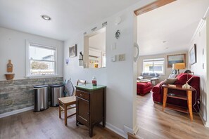 Una cocina compacta con ventana, un espejo y un rincón de comedor con un sofá rojo y una lámpara.