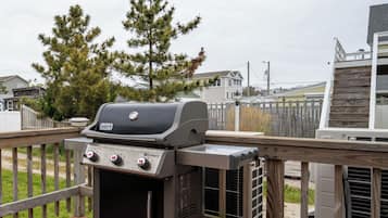 Een terras met een barbecue, omgeven door een houten hek en huizen op de achtergrond.