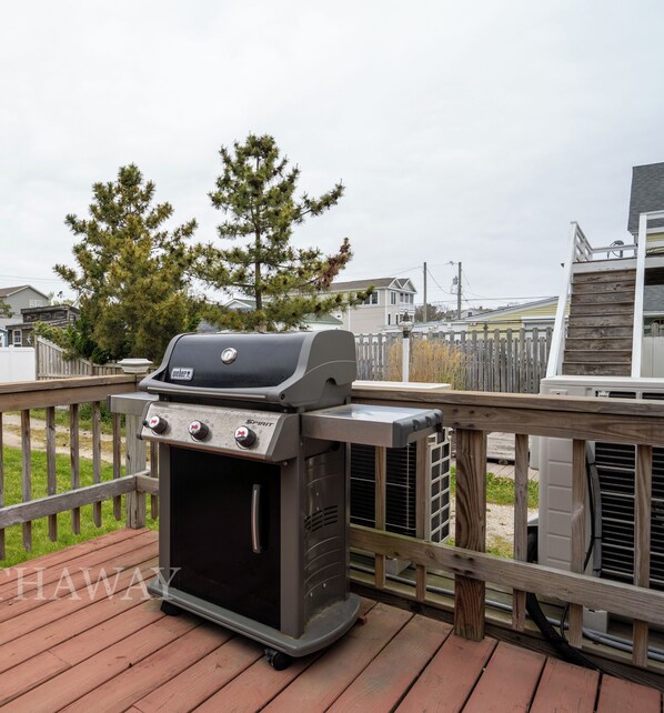 A deck with a barbecue grill, surrounded by a wooden fence and houses in the background.