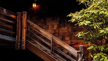 A wooden staircase leading to an upper level with a brick wall and a small tree.