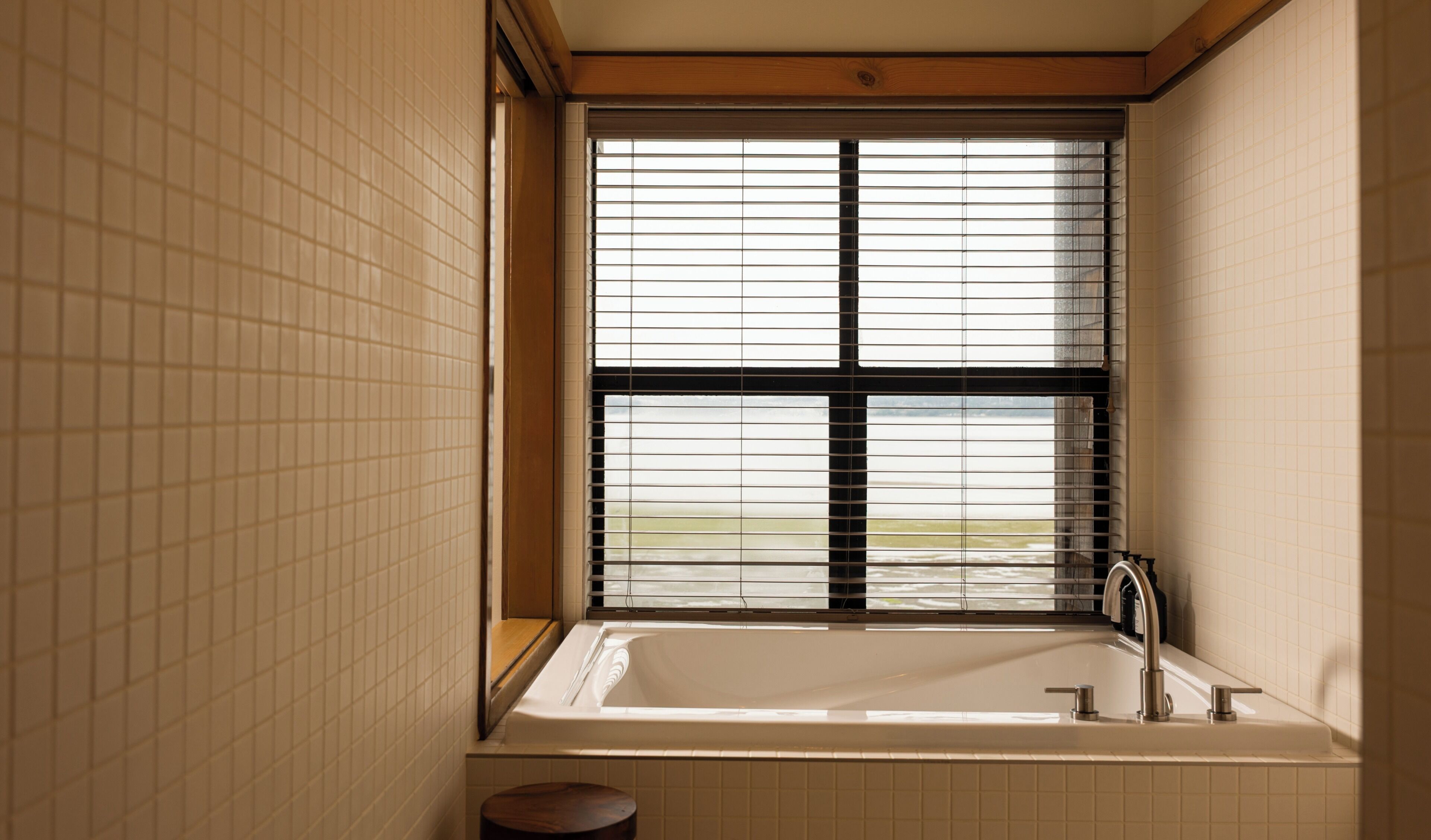 A bathroom with a bathtub, a window with blinds, and tiled walls.