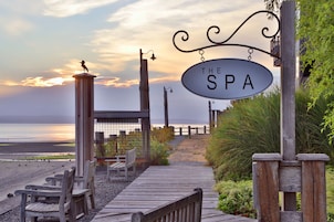 A wooden pathway leading to a spa sign with a view of the beach and ocean.