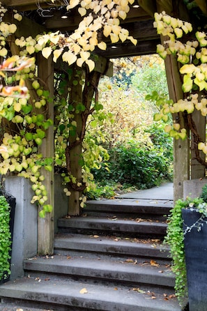 A stone staircase with a wooden pergola overhead, surrounded by greenery and a pathway leading into a garden. - The Inn at Langley (Langley)