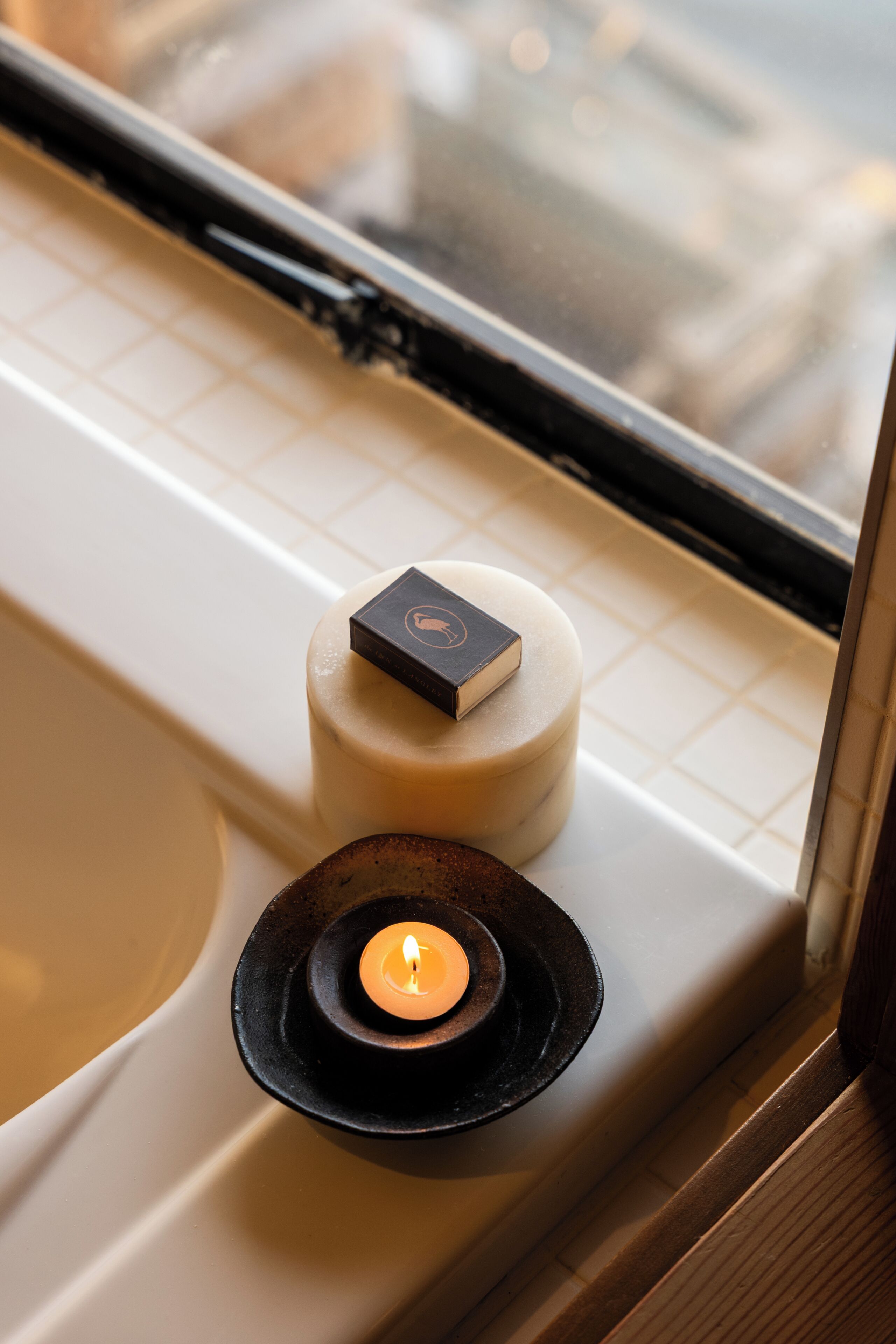 A candle on a black plate, a small box, and a round soap on a white surface.