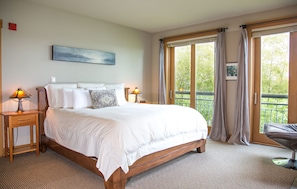 A bedroom with a large bed, two bedside tables with lamps, a painting on the wall, and a balcony with curtains.