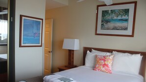 Una habitación de hotel con una cama, una mesita de noche con lámpara, un cuadro en la pared y una puerta que da a otra habitación.