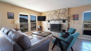 A living room with a stone fireplace, a sofa, a coffee table, and two armchairs. - Lajitas Casa Grande: Spacious Four Bedroom Home (Terilingua)