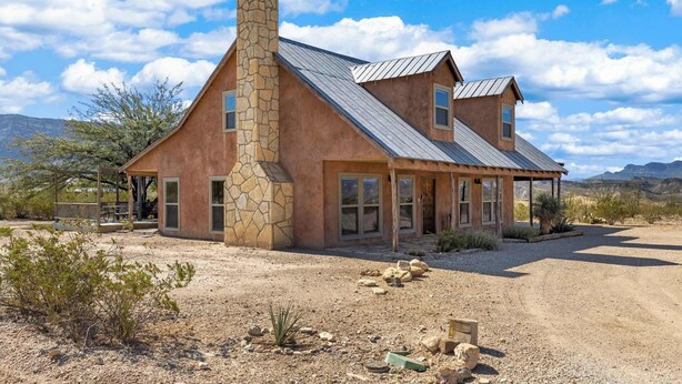 A two-story house with a stone chimney, large windows, and a covered porch. - Lajitas Casa Grande: Spacious Four Bedroom Home (Terilingua)