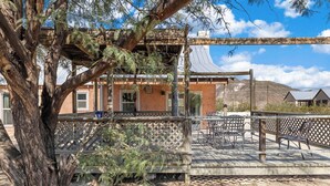 A rustic building with a wooden deck, outdoor seating, and a large tree in the foreground. - Lajitas Casa Grande: Spacious Four Bedroom Home (Terilingua)