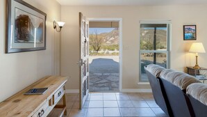 A room with a wooden bench, a framed picture, a lamp, and a view of a mountainous landscape through a door. - Lajitas Casa Grande: Spacious Four Bedroom Home (Terilingua)