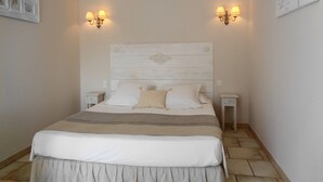 Un dormitorio con cabecera de madera, dos mesitas de noche, cama con ropa de cama blanca y color crema, y lámparas fijadas a la pared.