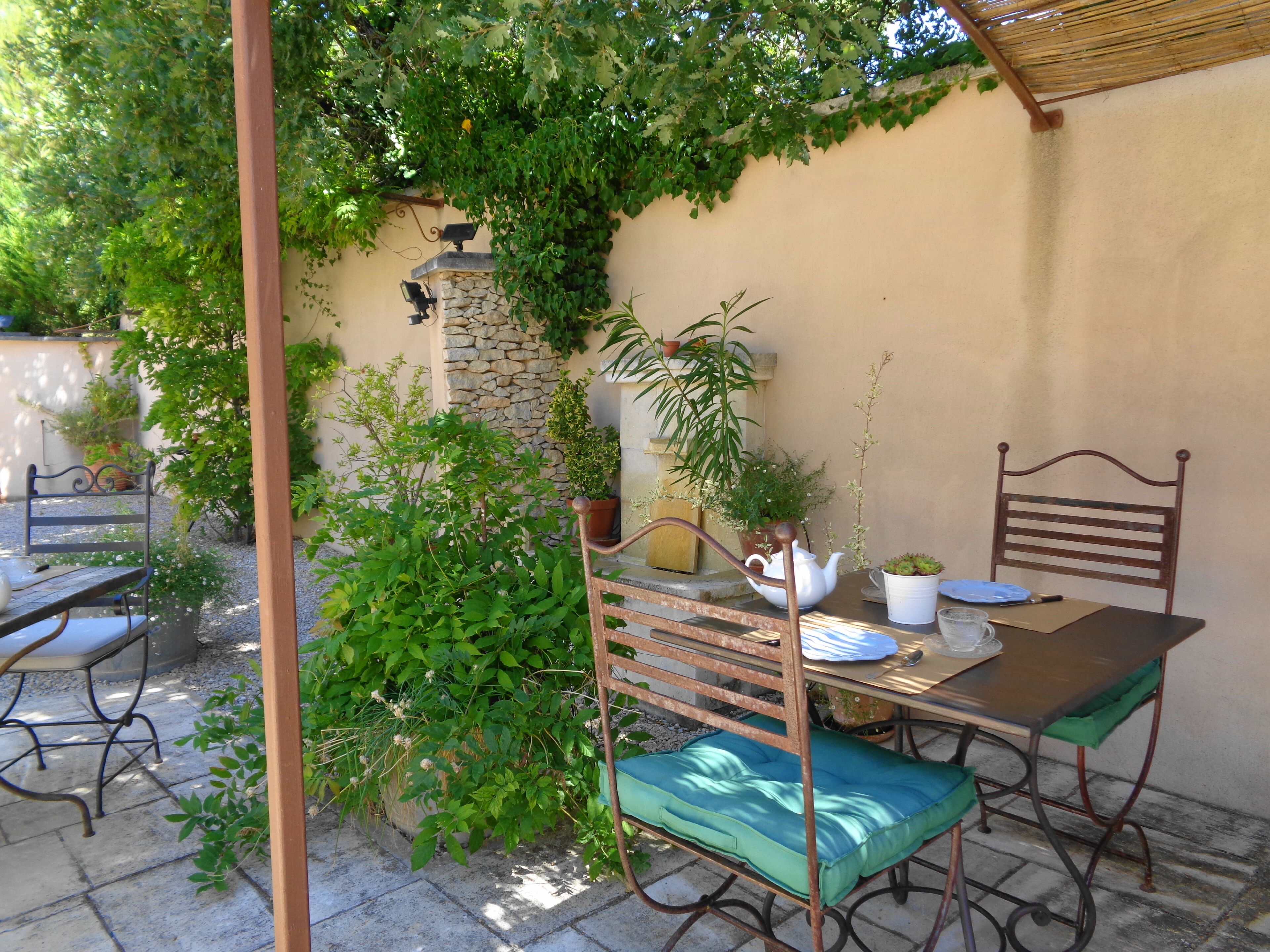 A patio with a table and chairs, surrounded by greenery and a stone wall.
