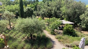 Un jardín con un camino de grava, varios árboles y una pequeña construcción con techo.