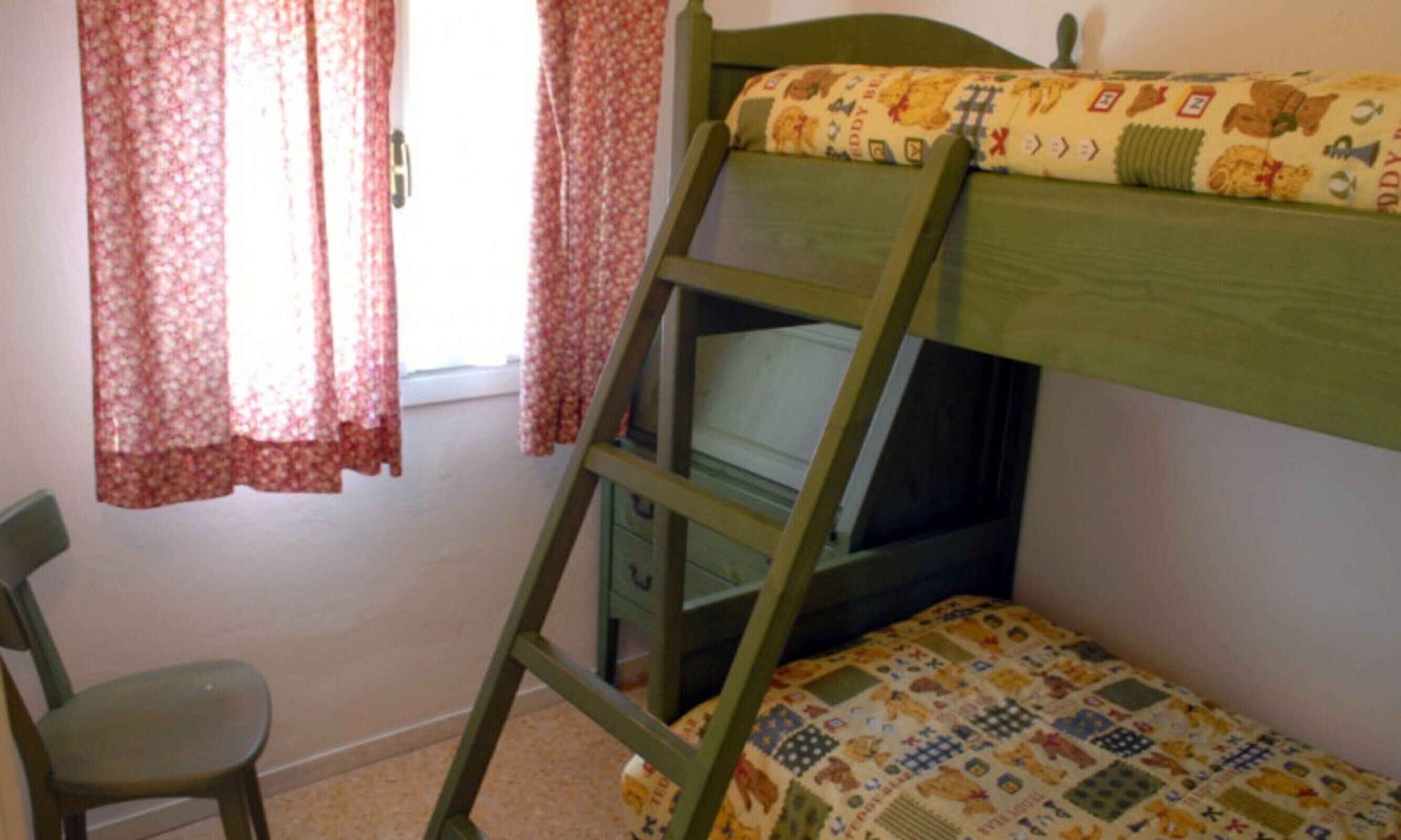 A bunk bed with a ladder, a chair, and a window with floral curtains.