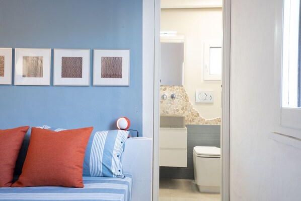 A bedroom with a bed, a bedside table with a lamp, and a bathroom visible through an open door.