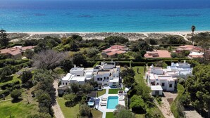 Un área residencial costera con casas modernas, una piscina y una playa al fondo.