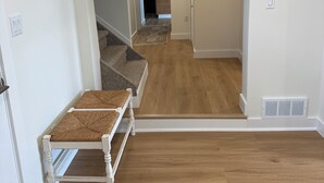 Um corredor com piso de madeira, paredes brancas e uma escada que dá para uma cozinha.