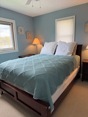 A bedroom with a bed, two bedside tables, a floor lamp, and a window with blinds.