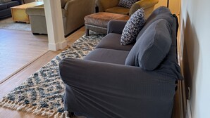 Uma sala de estar com um sofá cinza escuro, um tapete estampado e uma luminária.