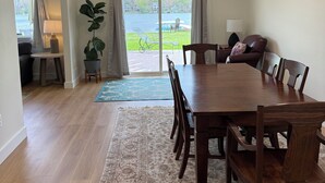 Uma sala de jantar ampla com uma grande mesa de madeira e cadeiras, uma planta em vaso e vista para um lago através de portas de vidro.