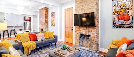 A living room with a fireplace, a television mounted on the wall, and a dining area in the background.