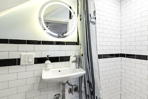 Une salle de bain avec un lavabo blanc, un miroir, un rideau de douche et des murs carrelés en noir et blanc.