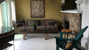 A living room with a stone fireplace, a sofa with cushions, a coffee table with decorative items, and a television mounted above the fireplace. - HIGH MOUNTAIN CONDO--PANORAMIC VIEWS! (Seven Devils)