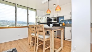 A modern kitchen with white cabinets, a wooden dining table, and two pendant lights. - Brand New And Fully Furnished 1 Bedroom Condo (Honolulu)