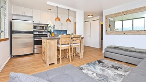 A modern kitchen with white cabinets, stainless steel appliances, and wooden chairs. - Brand New And Fully Furnished 1 Bedroom Condo (Honolulu)