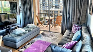 A living room with a grey sofa, a grey loveseat, a small table, and a balcony with a view of a residential building. - Brand New And Fully Furnished 1 Bedroom Condo (Honolulu)