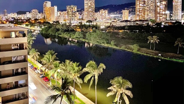 A nighttime cityscape with a river, palm trees, and high-rise buildings. - Brand New And Fully Furnished 1 Bedroom Condo (Honolulu)