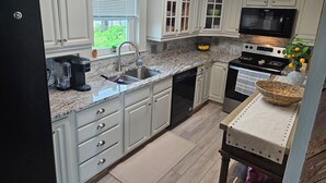 Una cocina con armarios blancos, un refrigerador negro, un microondas, una estufa y un fregadero.