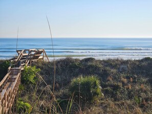 Ein hölzerner Steg führt zu einem Strand mit Blick auf den Ozean.